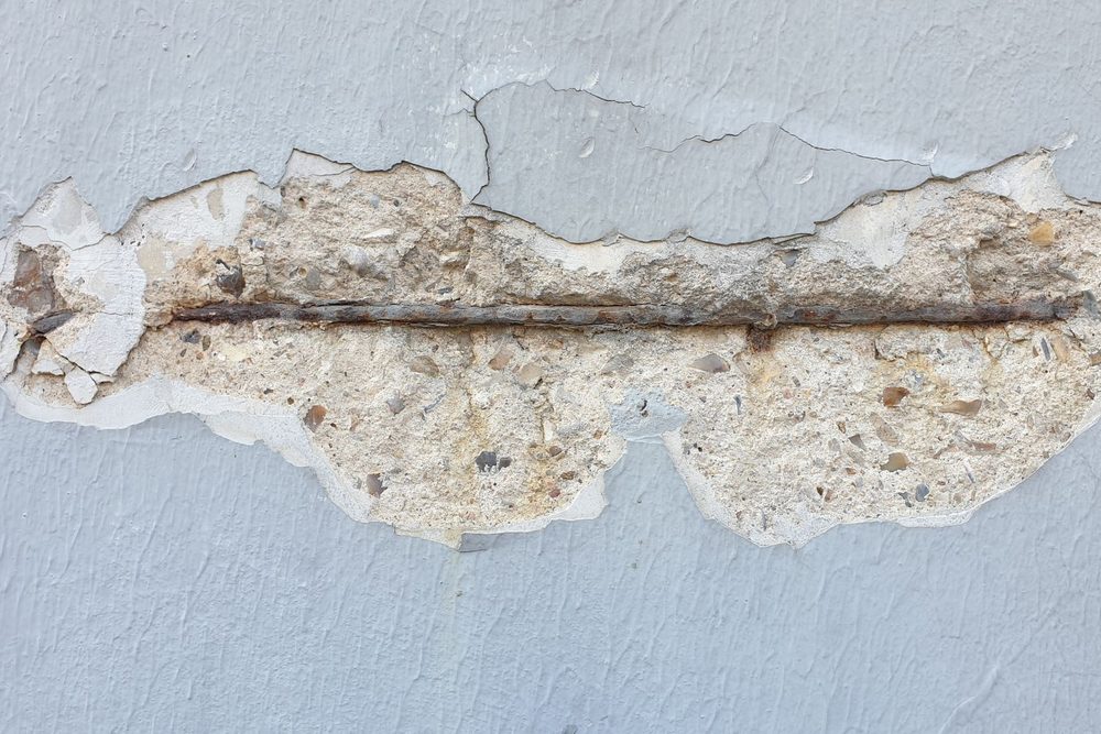 Béton éclaté sur une paroi enduite, laissant apparaître une barre d'armature rouillée