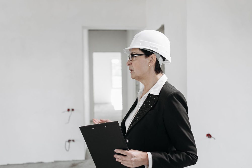 Contrôleuse en casque, porte-documents à la main, en visite dans un bâtiment en cours de travaux