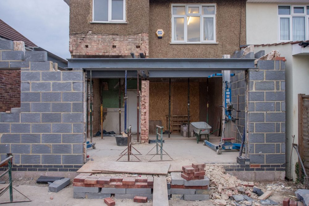 Façade arrière d'une maison en travaux : grande ouverture créée dans le mur, linteau métallique en place, extension en blocs de béton