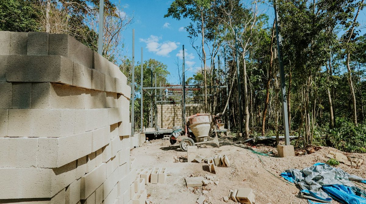 Murs en blocs de béton en cours d'élévation sur un chantier entouré de végétation, bétonnière et matériaux au pied des murs