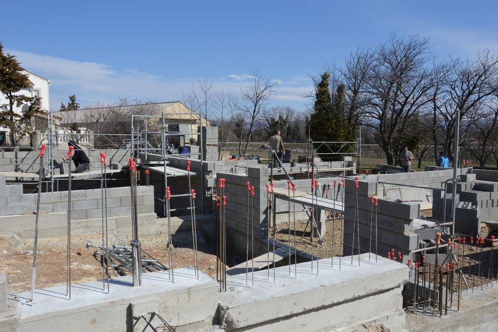 Fondations et premières rangées de blocs d'une construction, avec les armatures en attente des futurs poteaux et chaînages verticaux