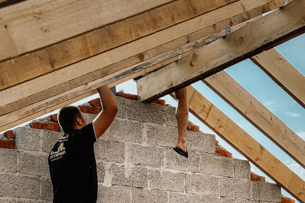 Charpentiers mettant en place les pièces d'une charpente bois au sommet de murs en blocs de béton