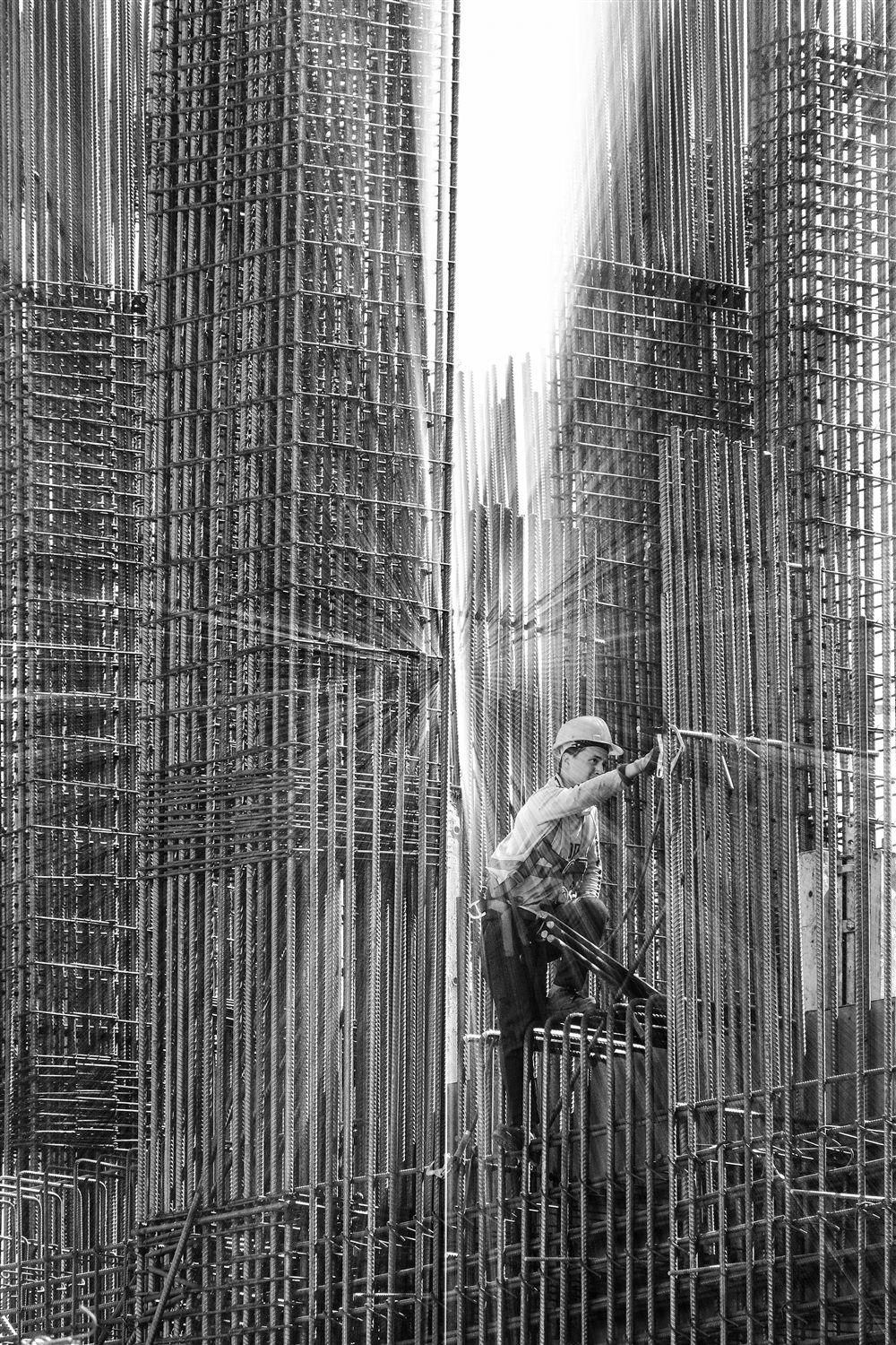 Ouvrier assemblant et ligaturant une cage d'armatures en acier pour un élément en béton armé sur un chantier