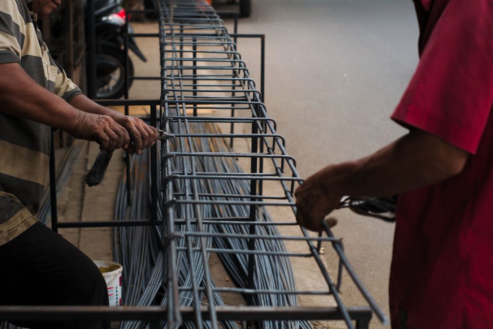 Ouvriers assemblant à la main une cage d'armatures longue de type longrine, cadres et barres filantes