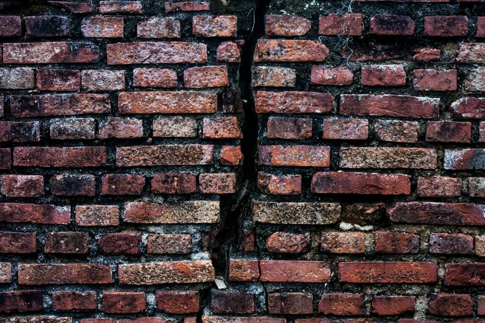 Fissure en escalier suivant les joints de briques sur un mur de maçonnerie ancienne