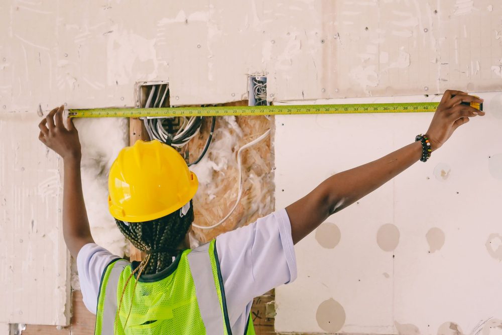 Relevé au mètre ruban d'un mur existant mis à nu, en cours de rénovation, par une personne en casque et gilet