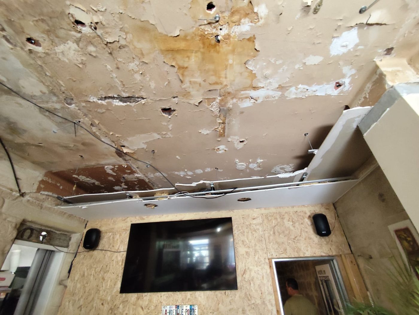 Plafond au-dessus de l'écran mural : plâtre écaillé et poutre encastrée dans le mur en pierre